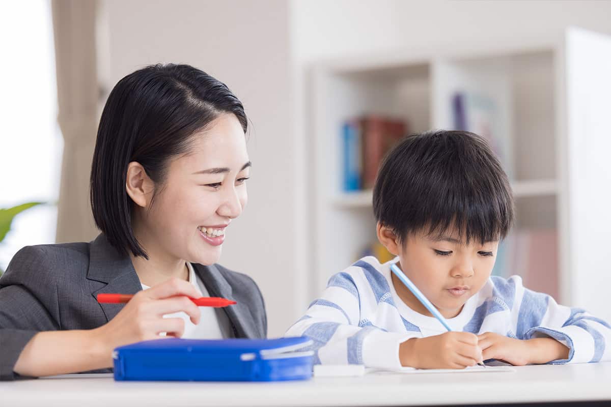 小学生の男の子の勉強を見守る女性講師